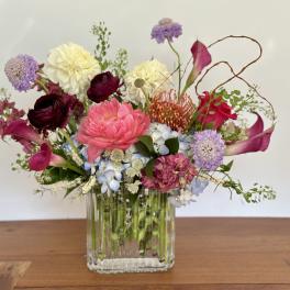 Mixed bouquet in a clear glass vase with pink, purple, white, and blue flowers