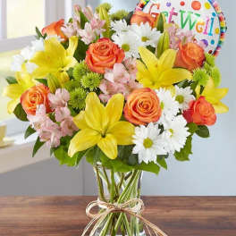 Mixed bouquet of yellow lilies, orange roses, and white daisies in a glass vase