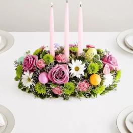 Pink floral centerpiece with three tall candles on a table
