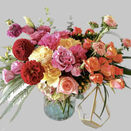 Mixed bouquet of roses, dahlias, and other blooms in a glass vase