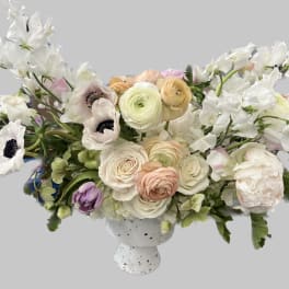 White and blush floral arrangement in a speckled pedestal vase