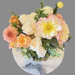 Bouquet of cream, peach, and pink flowers in a round white vase