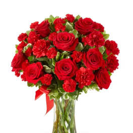 Red roses and carnations in a clear glass vase with a red ribbon
