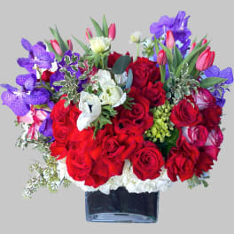 Red roses and purple orchids in a square glass vase