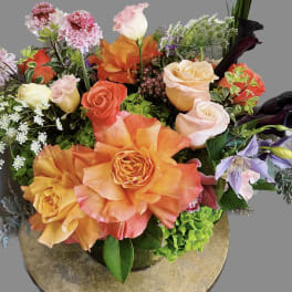 Mixed bouquet of orange, pink, and cream roses with purple blooms in a vase