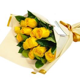 Bouquet of yellow roses wrapped in cream paper with a gold ribbon