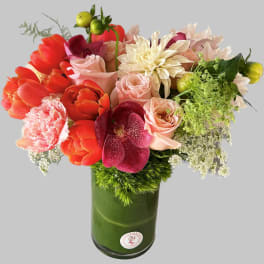 Mixed bouquet in a green glass vase with tulips, roses, and orchids
