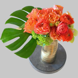 Orange and pink bouquet in a metallic vase with large tropical leaves
