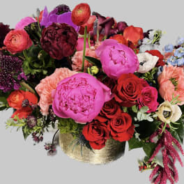 Mixed bouquet of bright pink, red, and purple flowers in a gold vase