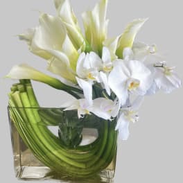 White calla lilies and orchids in a square glass vase