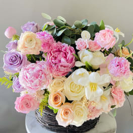 Mixed pastel bouquet in a black basket with roses and peonies
