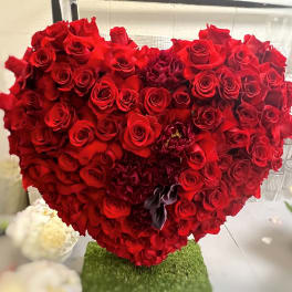 Heart-shaped arrangement of red roses with a few dark accent flowers