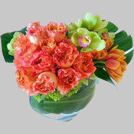 Bouquet of orange carnations and green orchids in a glass vase