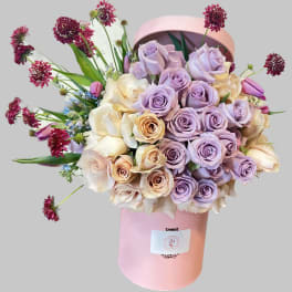 Lavender and cream rose bouquet in a pink hatbox with burgundy accent flowers