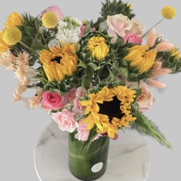 Bouquet of sunflowers, pink roses, and carnations in a green glass vase