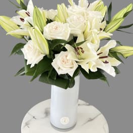 White roses and lilies arranged in a tall white vase.