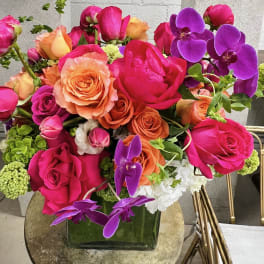 Bright bouquet of pink, orange, and purple roses in a square glass vase