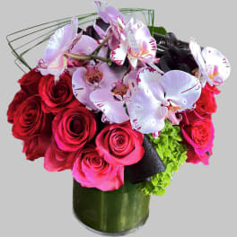 Bouquet of red roses and pink orchids in a green glass vase