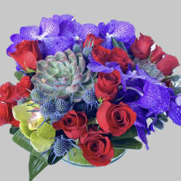 Bouquet of red roses, purple orchids, and succulents in a glass vase