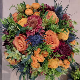Bouquet of orange roses, burgundy blooms, and blue thistles