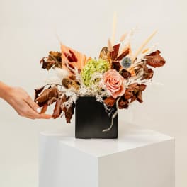 Arrangement of a peach rose and dried flowers in a black vase