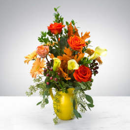 Orange roses and calla lilies in a yellow vase with autumn foliage