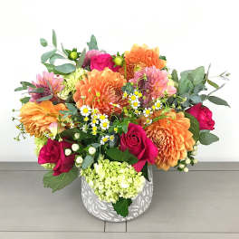 Colorful bouquet of roses, dahlias, and small daisies in a patterned vase