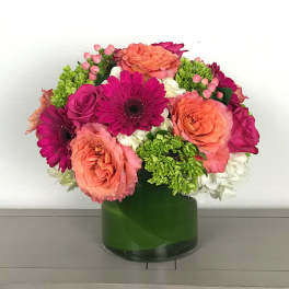 Mixed pink and coral flowers arranged in a green glass vase
