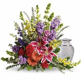 Mixed bouquet with pink lilies, roses, and purple flowers beside a silver urn