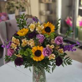 Mixed bouquet of sunflowers, purple roses, and alstroemeria in a glass vase