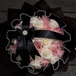 Bouquet of pink and white roses wrapped in black paper with a satin bow