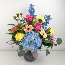 Mixed bouquet with blue hydrangea, pink roses, and yellow carnations in a glass vase