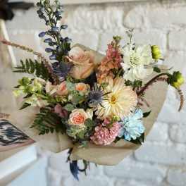 Hand-tied bouquet of pastel flowers wrapped in brown paper