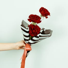 Three red roses wrapped in striped paper with a ribbon