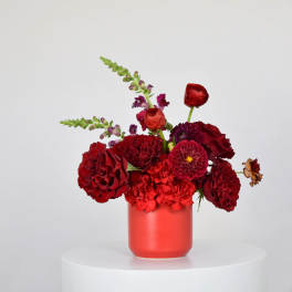 Red floral arrangement in a coral vase with mixed blooms
