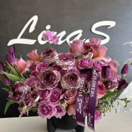 Pink and purple bouquet in a black vase with ribbon tags