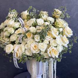 Cream rose arrangement in a white urn with trailing white accents