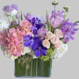 Pink roses and purple orchids arranged in a square glass vase
