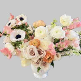 Bouquet of cream, peach, and pink flowers in a white vase