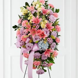 Standing spray of pink lilies, lavender roses, and carnations on an easel with lavender ribbon.