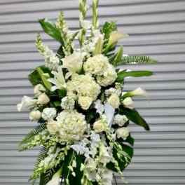 Tall white standing spray of mixed flowers and large tropical leaves on an easel.
