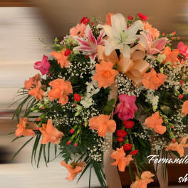 Large peach and pink flower arrangement with lilies, roses, and a ribbon bow