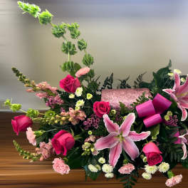 Pink lilies and roses arranged around a pink keepsake box with Bells of Ireland accents