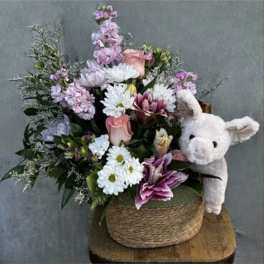 Mixed pastel flower arrangement in a woven basket with a plush pig
