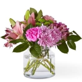Pink lilies and purple flowers in a clear glass vase