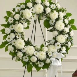White floral wreath on a black stand with a white ribbon