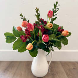Pink and peach tulips with red blooms in a white vase