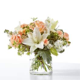 Peach roses and white lilies in a clear glass vase