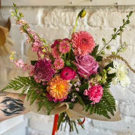 Hand-tied bouquet of pink, orange, and white flowers wrapped in paper