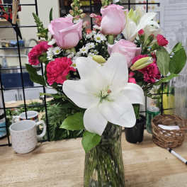 Pink roses and carnations with a large white lily in a glass vase